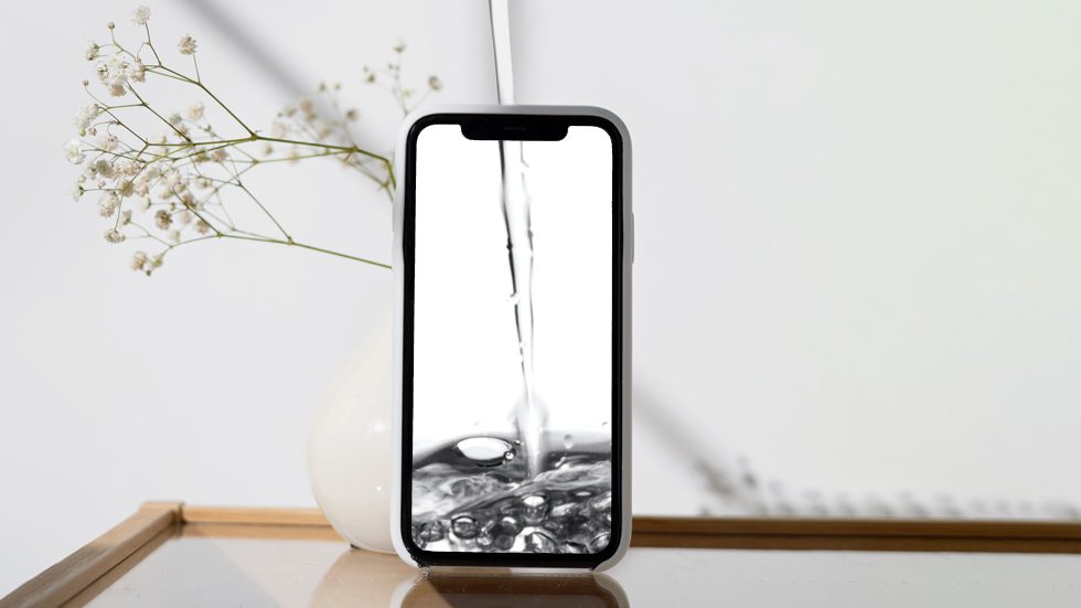 Blog hero image: Pouring from the top, water appearing to fill up the white empty screen of a mobile phone screen. Background is a serene, well-lit room, the top of a wood table and a plant and shadow diagonal from to the left.